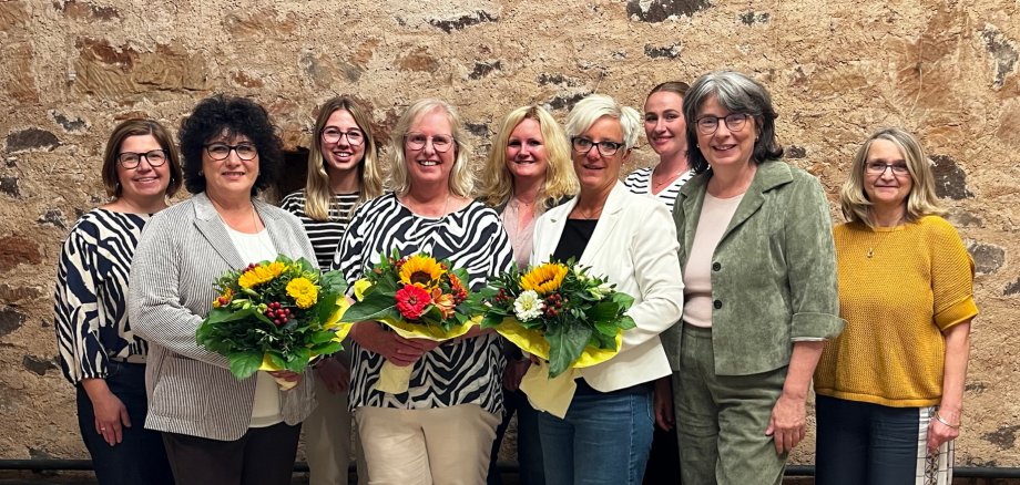 Frauengruppe vor einer Sandsteinwand bei einer Ehrung, drei davon mit bunten Blumensträußen