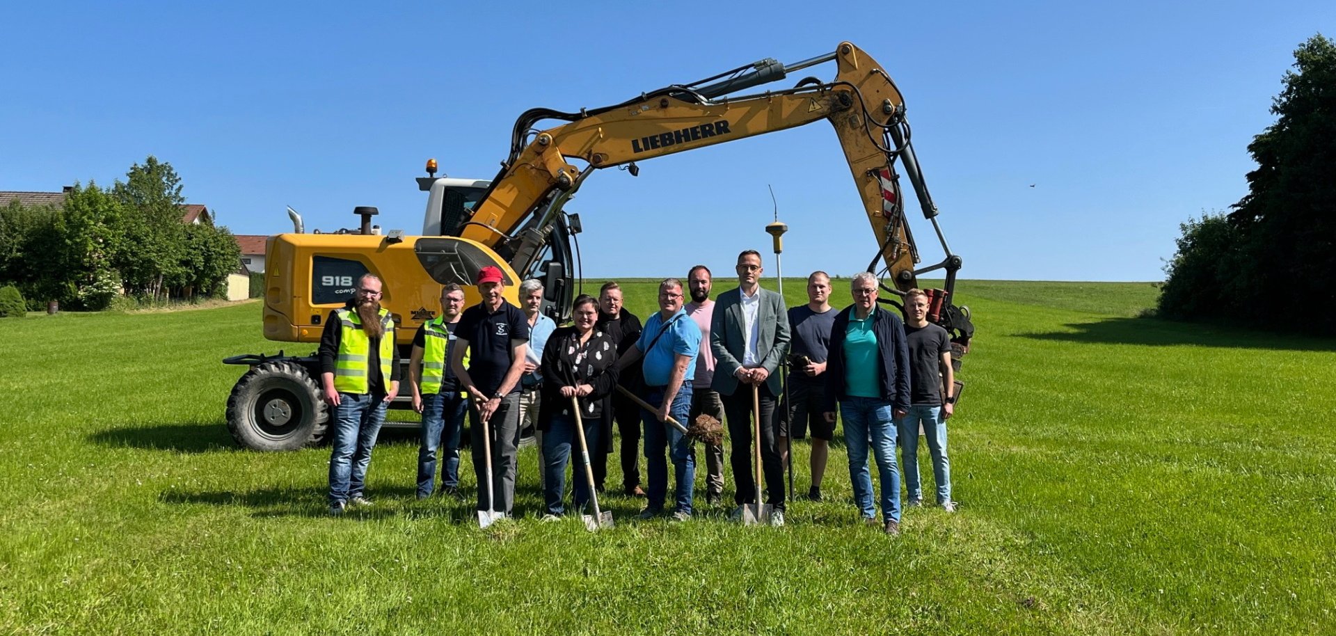 Menschengruppe auf einer Wiese vor einem Bagger