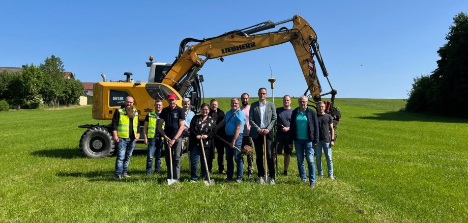 Menschengruppe auf einer Wiese vor einem Bagger