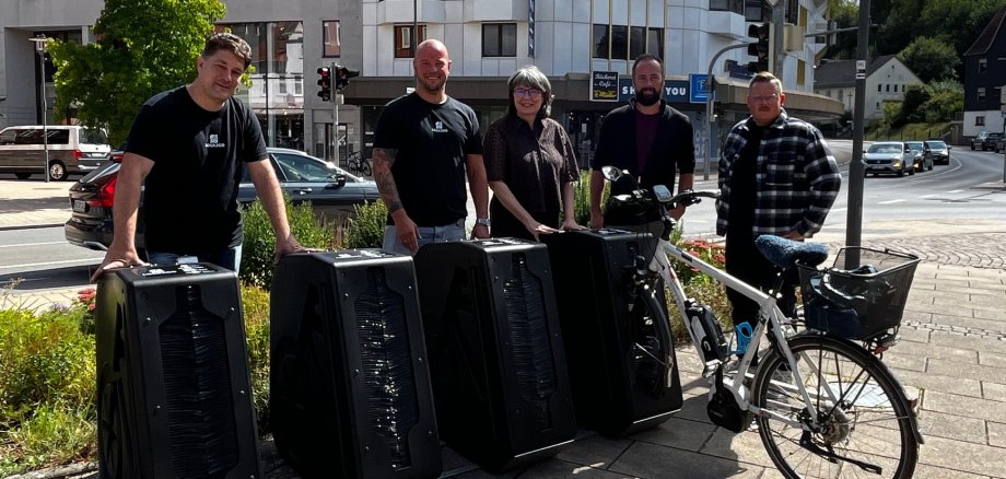 Fünf Personen hinter schwarzen Fahrradabstellboxen sowie ein Fahrrad