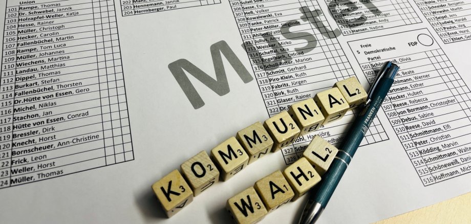 Musterwahlzettel mit einem Stift und aus Buchstabenwürfeln gelegt das Wort Kommunalwahl