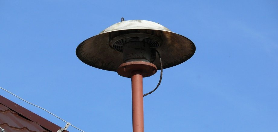 Sirene auf einem Hausdach vor blauem Himmel