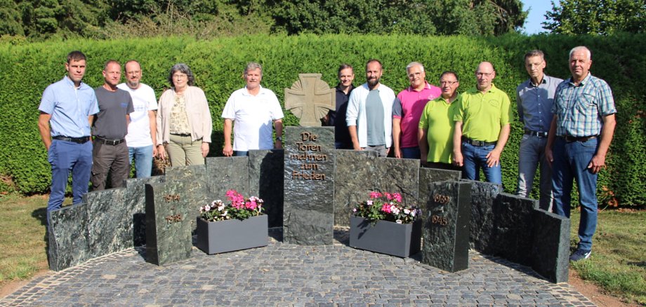 Menschengruppe im Halbkreis hinter einem steinernen Kriegsopfer-Ehrenmal 