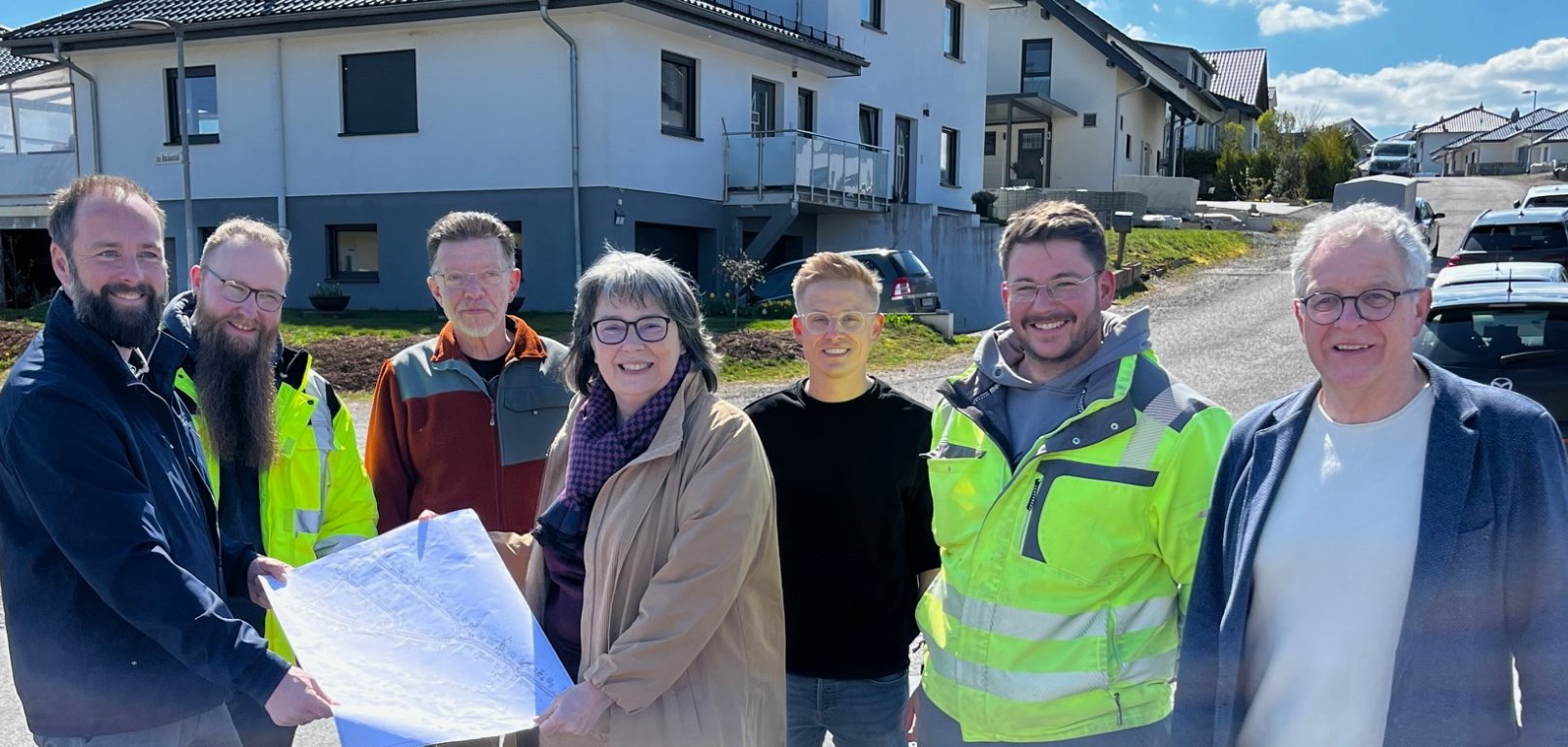 Gruppe von Personen zum Teil mit Sicherheitswesten auf einer Straßenkreuzung vor einem Haus