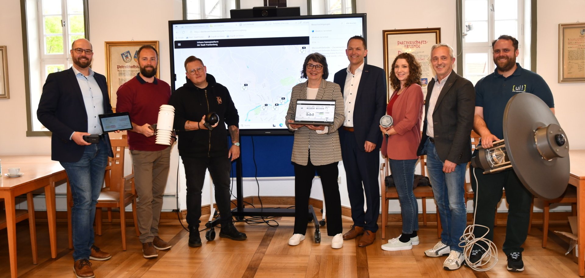 Mehrere Personen im Halbkreis vor einem Präsentationsboard mit verschiedenen Mobilgeräten