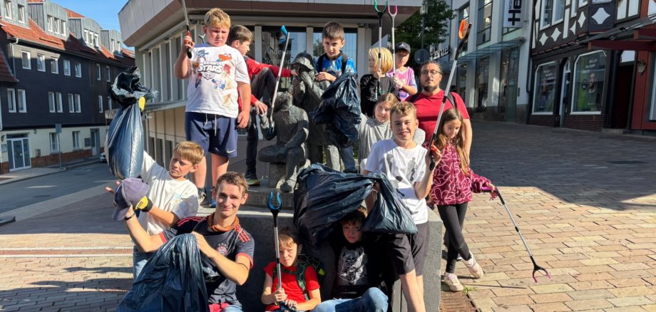 Gruppe von Kinder und Jugendlichen mit Greifzangen und Müllsäcken, die sich um eine Bronzeskulptur angeordnet haben