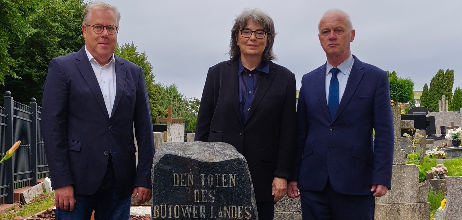 Eine Frau und zwei Männer in schwarzer Kleidung am Ehrenmal für die Toten des Zweiten Weltkriegs.