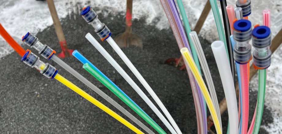 Bunte Glasfaserleitungen die aus einem Kieshaufen herausschauen