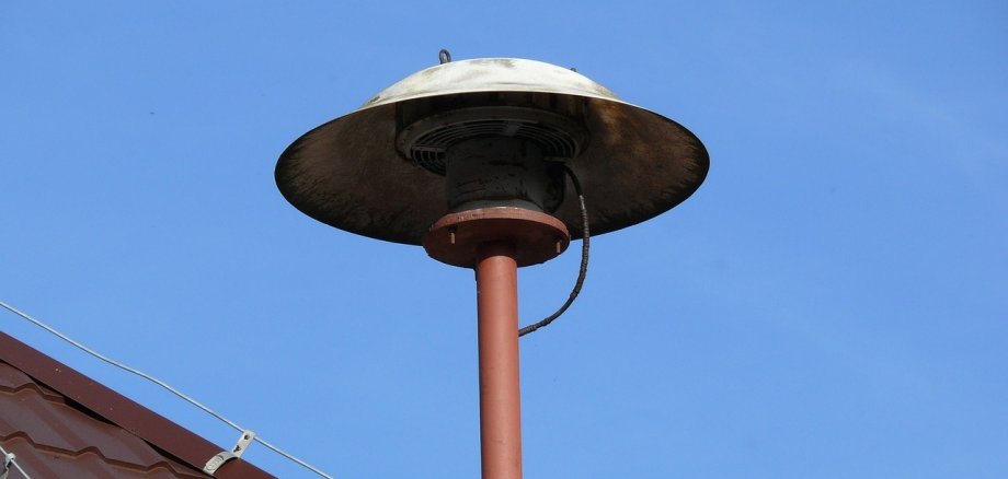 An einem Hausdach montierte Sirene vor blauem Himmel