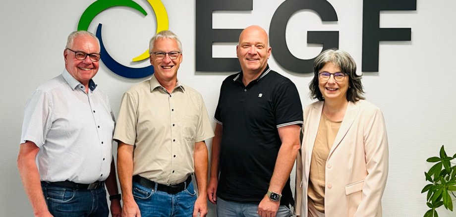 Drei Männer und eine Frau stehen vor einem großen EGF-Logo an der Wand