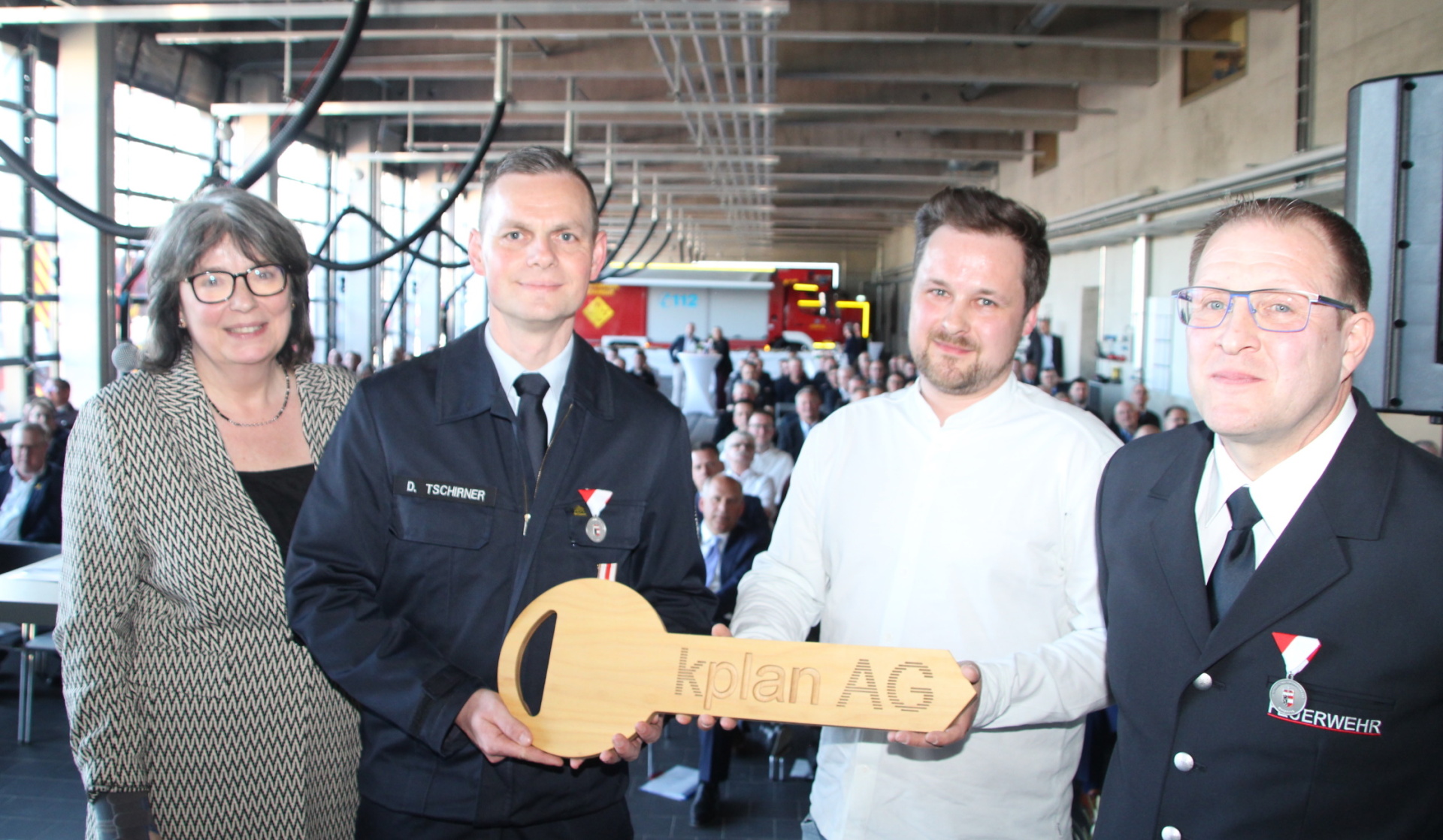 Vier Personen mit einem großen Holzschlüssel in einer Fahrzeughalle