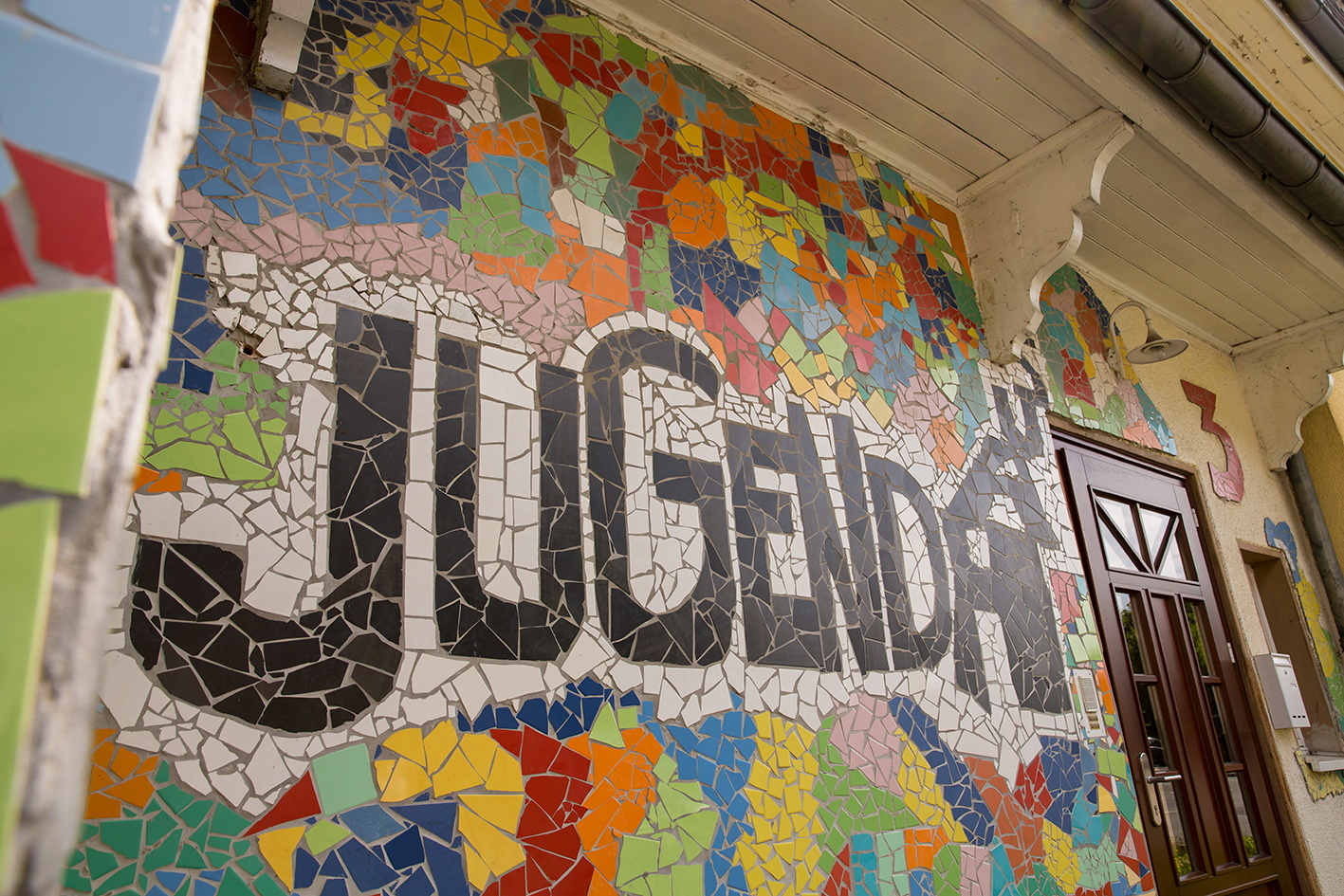 Schwarzer Schriftzug Jugendhaus auf einer bunten Mosaikwand