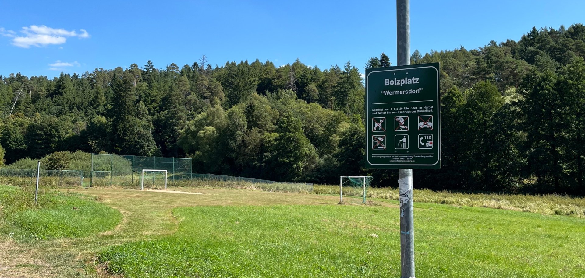 Laternenmast mit einem Bolzplatzschild vor einer Wiese mit zwei Spieltoren