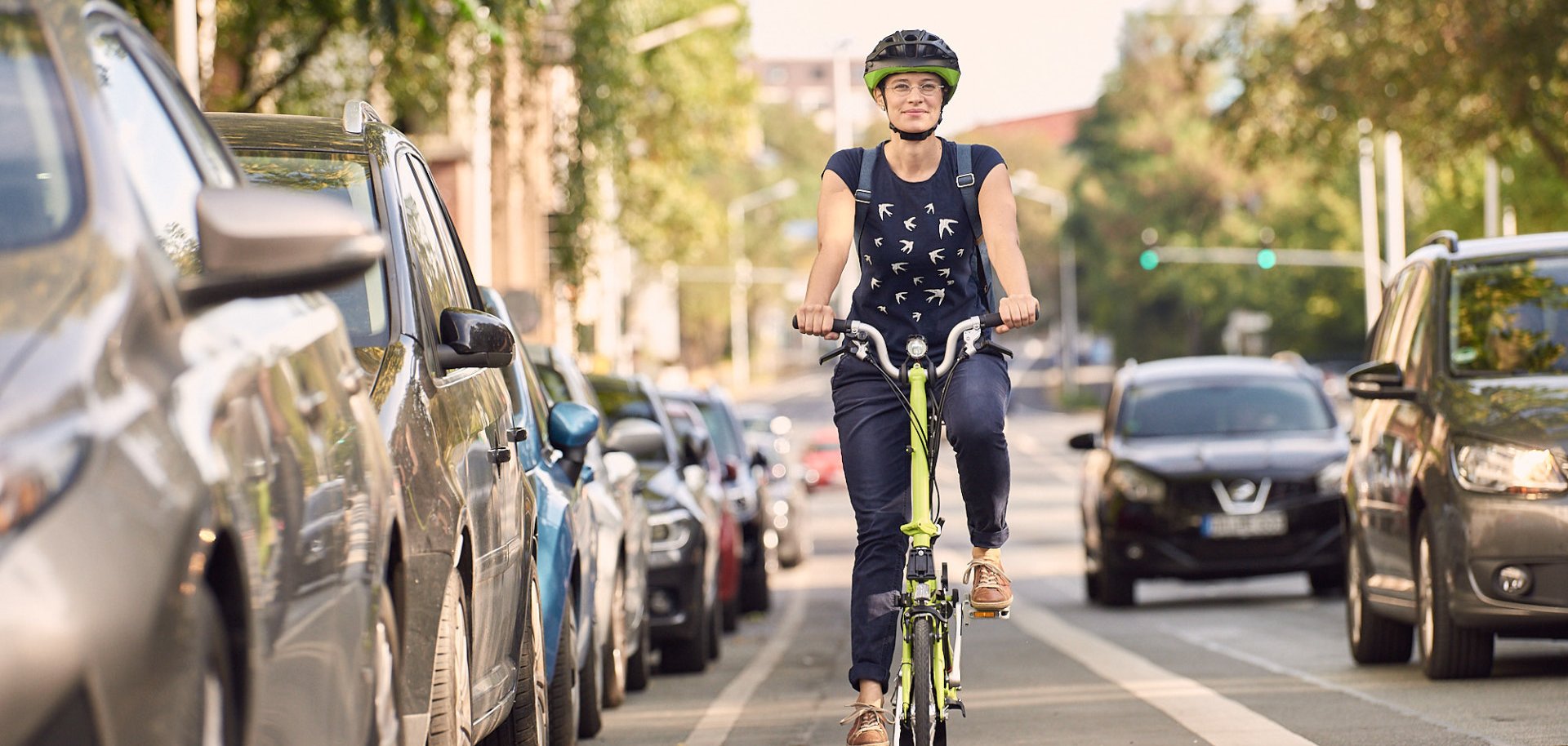 Fahrende Radfahrerin auf einem Radweg zwischen parkenden Autos und Autoverkehr