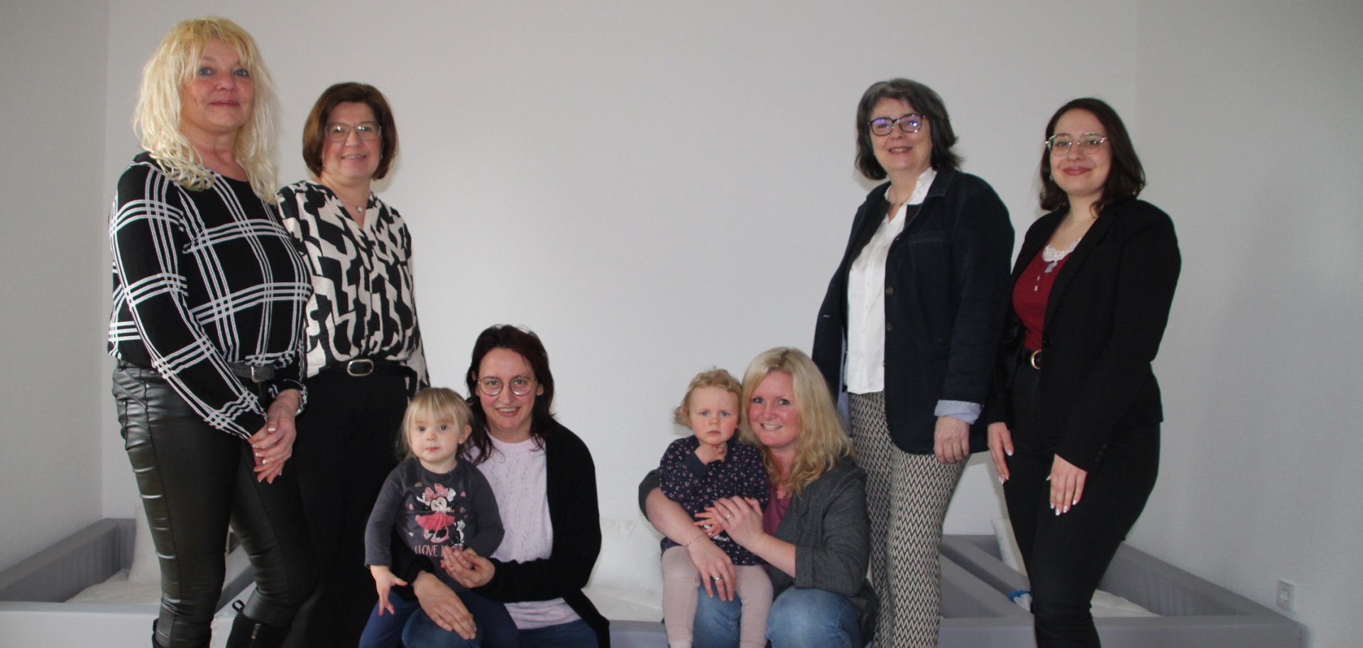 Mehrere Frauen und zwei Kleinkinder in einem Krippen-Schlafraum hinter einem Kinderbett