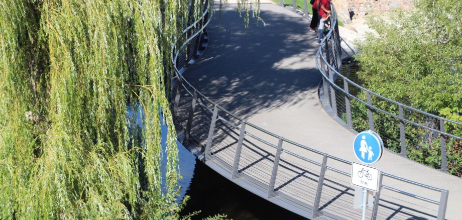 Geschwungene Radverkehrsbrücke über ein Gewässer aus der Vogelperspektive