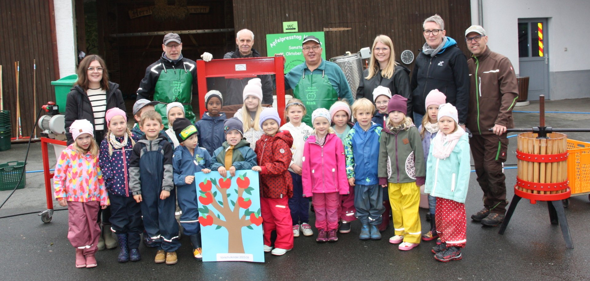 Kindergartengruppe mit Betreuenden vor einer Apfelpresse
