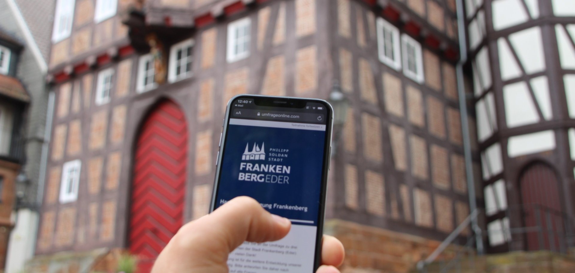 Smartphone in einer Hand vor dem Historischen Rathaus