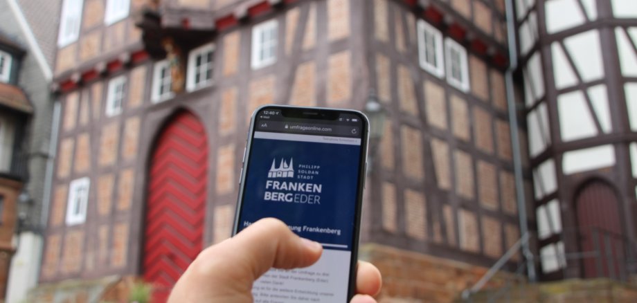 Smartphone in einer Hand vor dem Historischen Rathaus