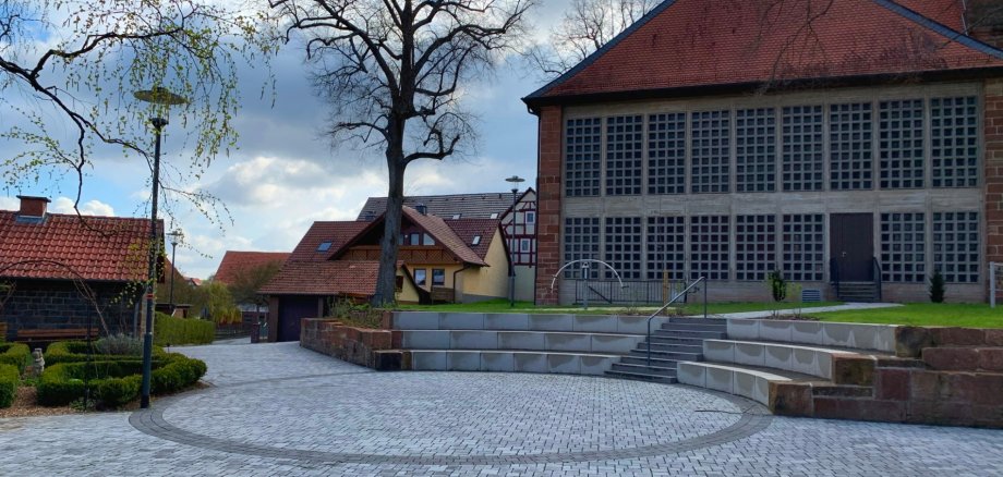 Ein grau gepflasterter Platz, darum Bäume und ein Kirchenbau